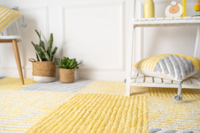 A yellow and grey striped cushion with vertical, and horizontal stripes, adorned with tassels on each corner, in a modern space with a butterfly rug.