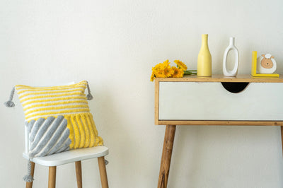 A yellow and grey striped cushion with vertical, and horizontal stripes, adorned with tassels on each corner, in a modern space with a butterfly rug.